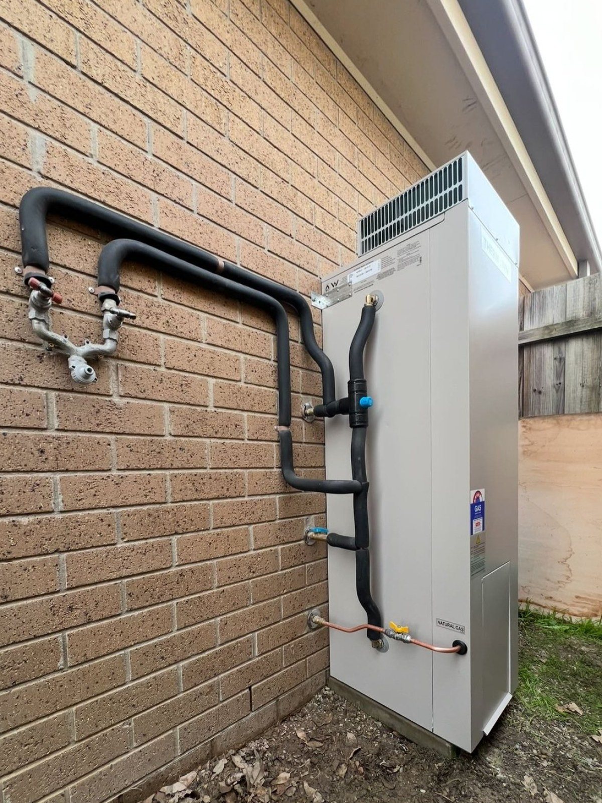 Storage hot water unit beside a brick wall with lagged pipework
