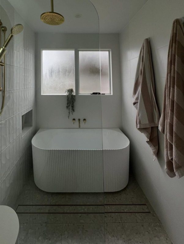 Finished bathroom with a freestanding fluted bath, wall mounted brass bath spout and a brass overhead shower