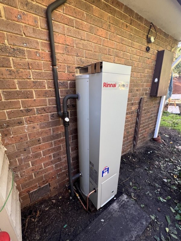 Rinnai gas storage hot water unit against a brick wall with a relief drain line and copper connections at the base